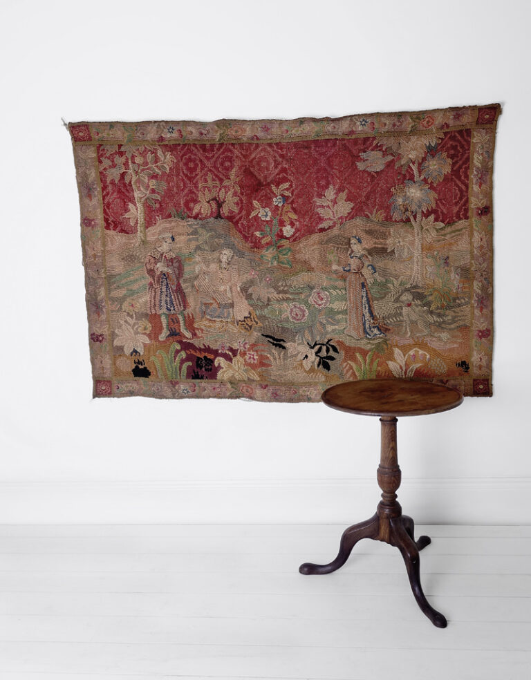 A large antique handwoven woolen tapestry depicting three medieval characters and a dog. Surrounded by trees and flowers and a single bird in flight.